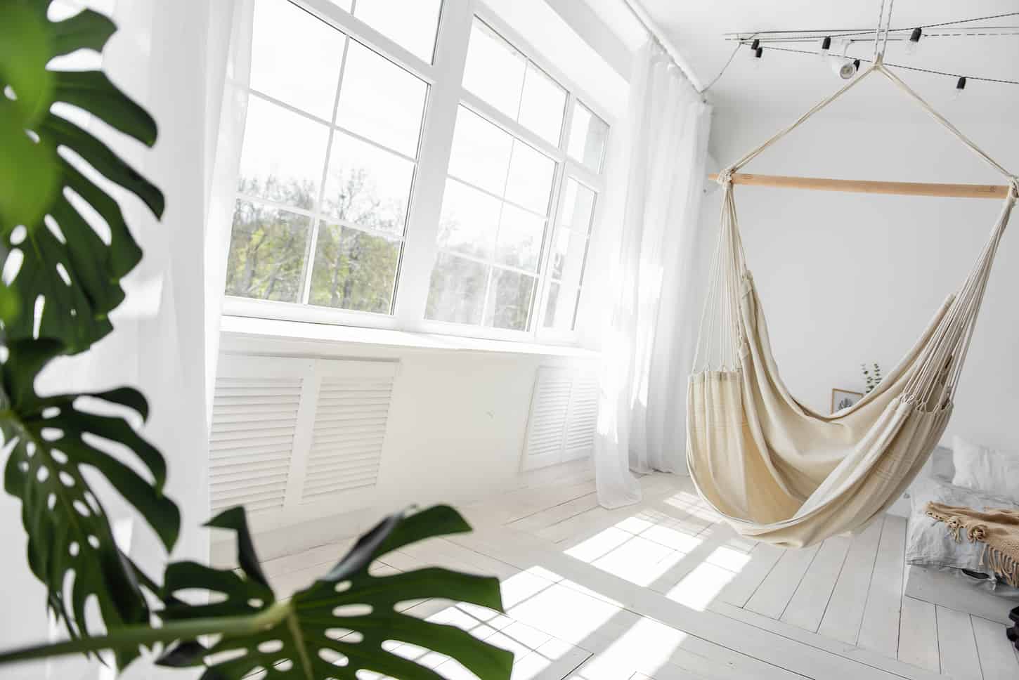An image of a Stylish, trendy interior in Scandinavian style. A large wooden window sees a white macrame hammock.