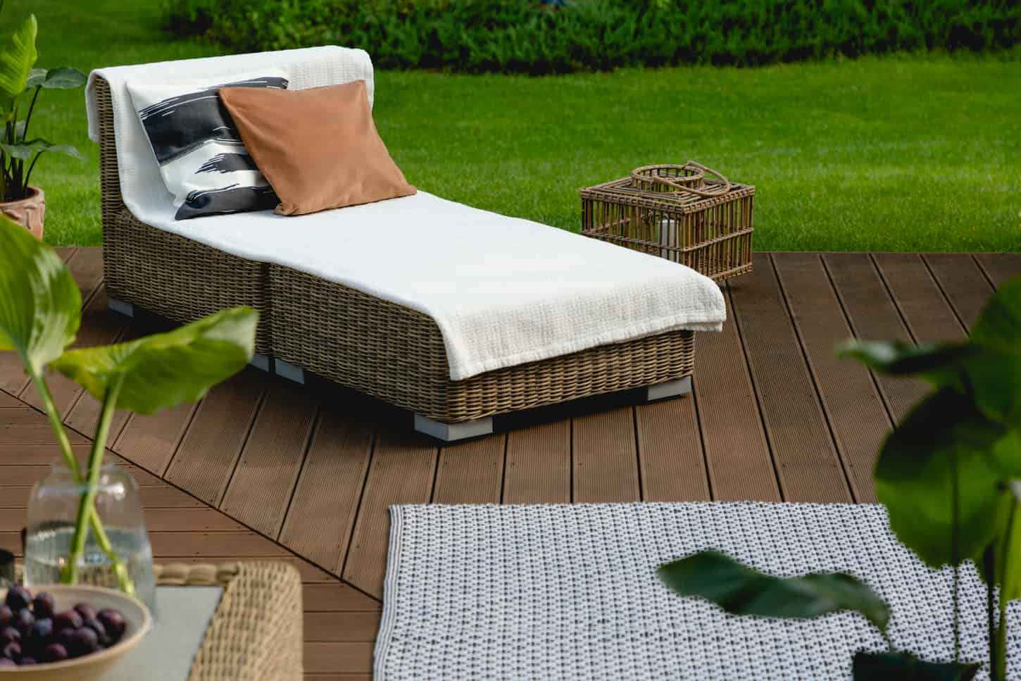 An image of a Wooden deck in green garden with rattan furniture and an outdoor rug.