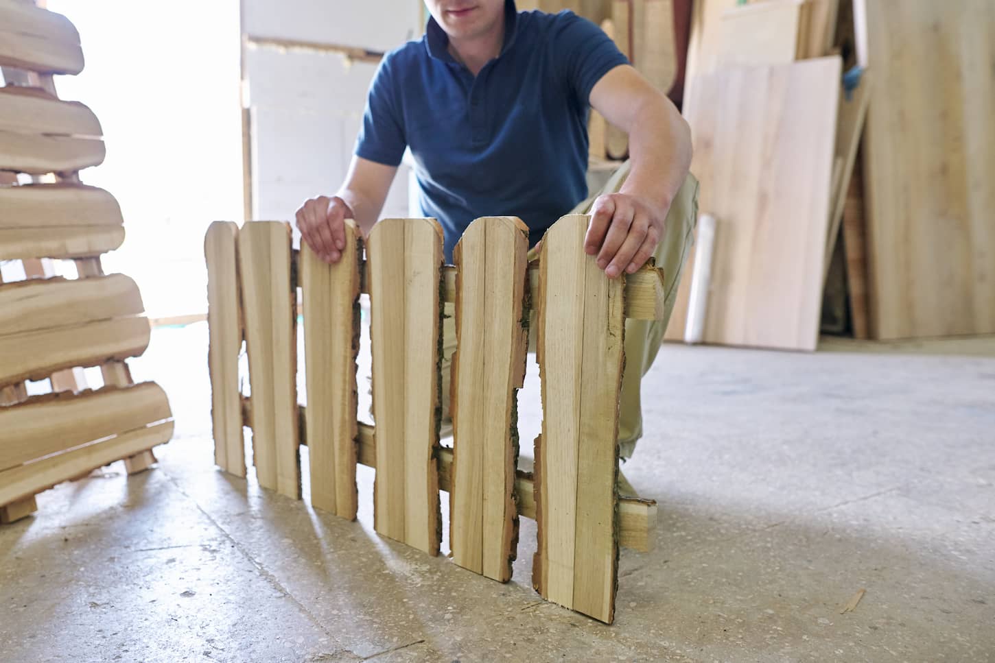 An image of a Male carpenter showing new made wooden low fence in carpentry at a woodworking workshop, a woodworking machinery background, short fence in natural country style.
