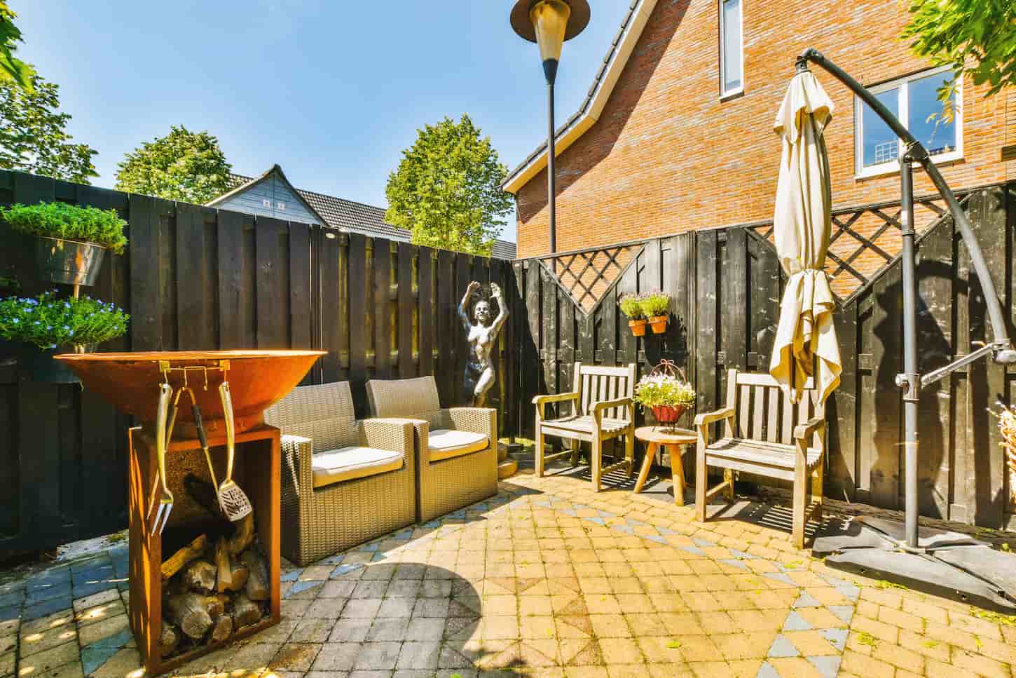 An image of a Neatly paved patio with sitting area and small garden near wooden fence.
