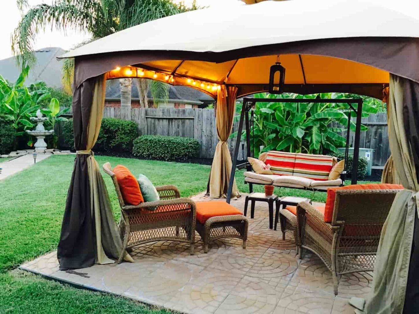 An image of an Outdoor covered gazebo with lighting and striking patio furniture; features a stone fountain.