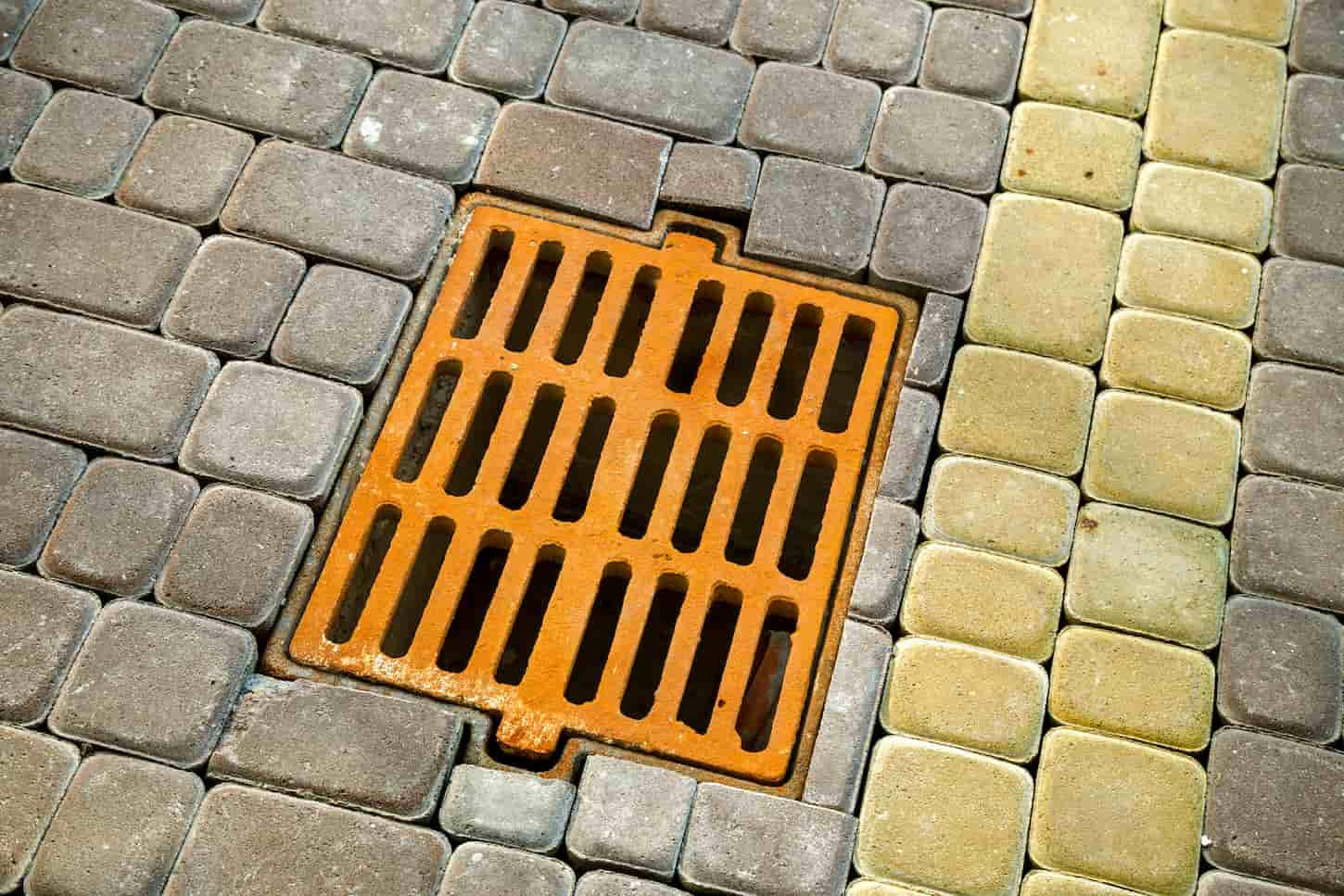 An image of an Old rusted metal gutter for rainwater on the stone-paved sidewalk.