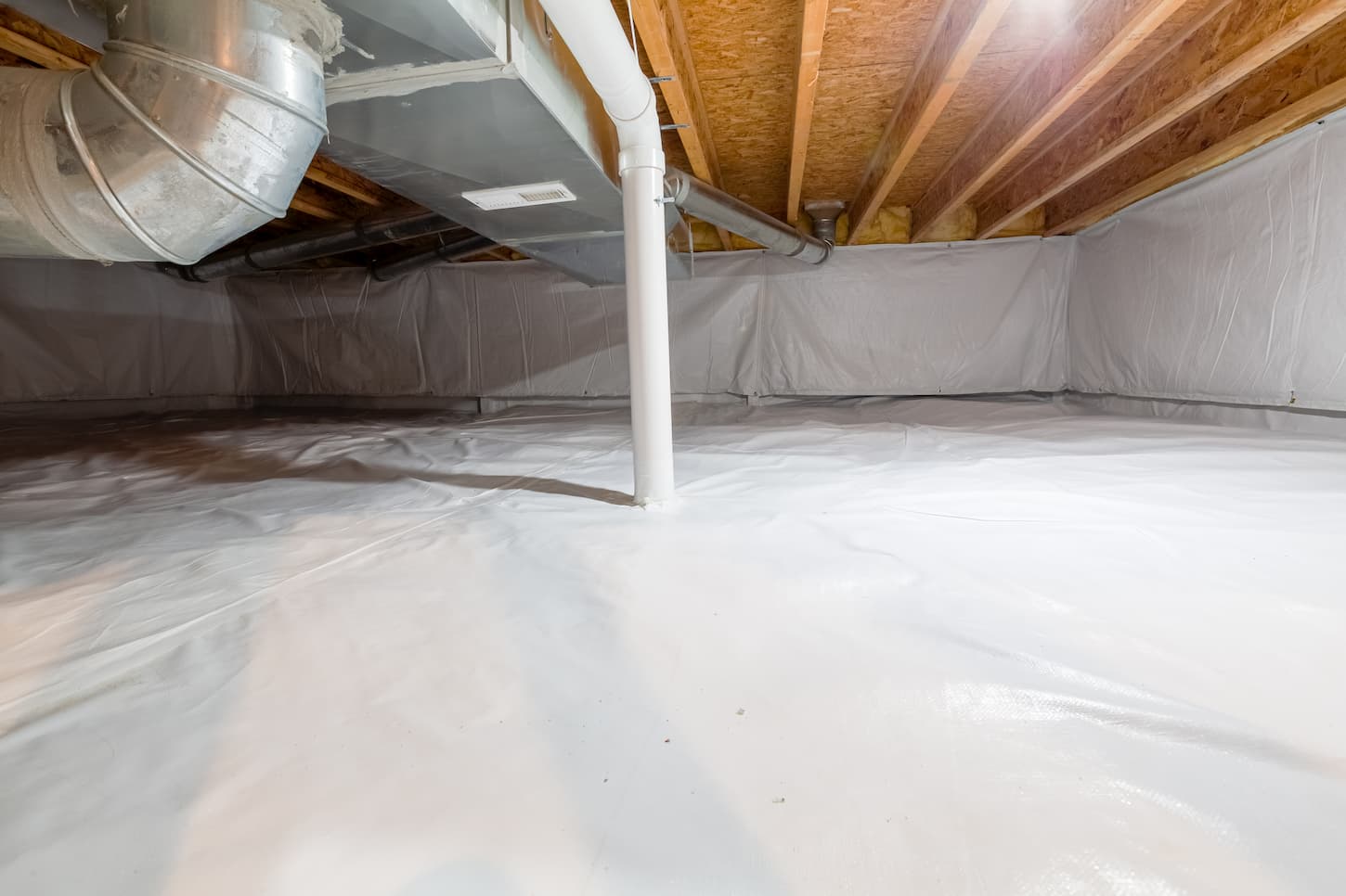 An image of a Crawl space fully encapsulated with thermoregulatory blankets and dimple board. Radon mitigation system pipes visible. Basement location for energy-saving home improvement concept.