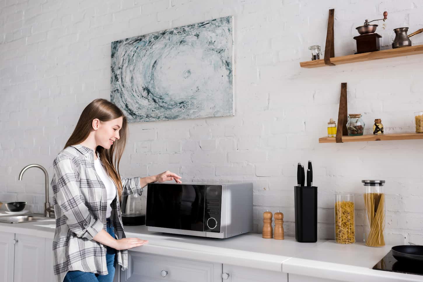 An image of a smiling woman looking at the microwave in kitchen.