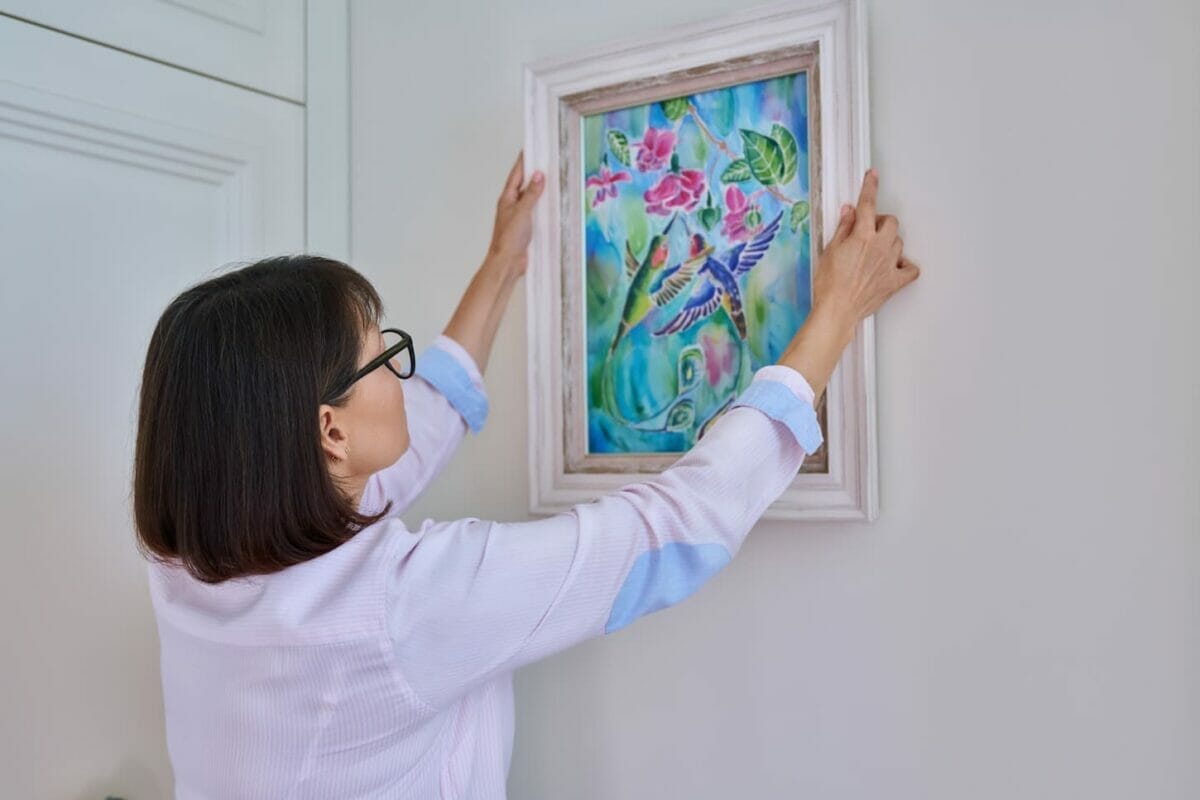 An image of a Woman hanging floral birds art framed at home on the wall.